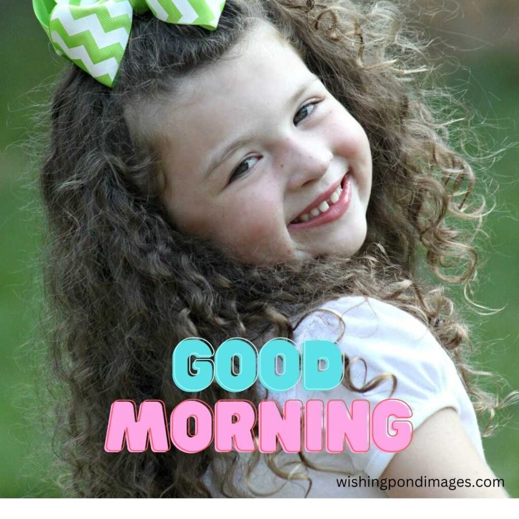 A baby girl in the morning with a beautiful smiling face wearing a white top with loose hair and a green bow-type hair band