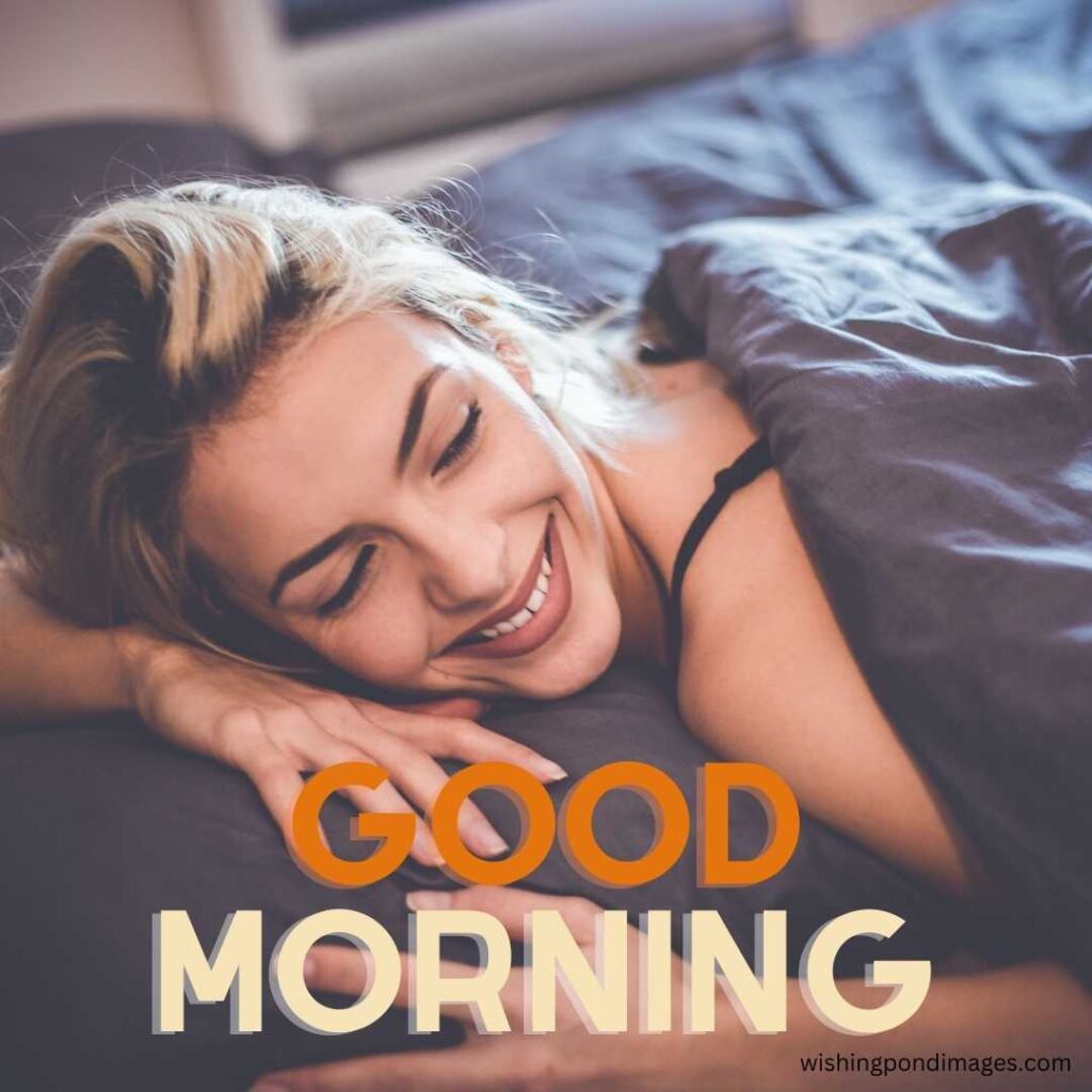 A young blonde-haired girl smiling and resting her head on a pillow in the morning