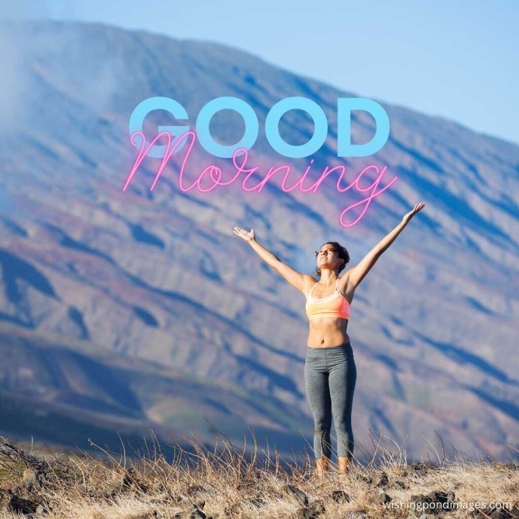 A young girl standing and raising her both arms upwards wearing a short sleeveless top and skin-fit leggings near the mountain in the park in the morning