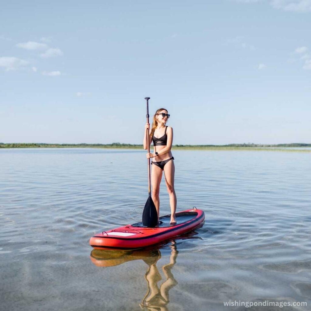 A young girl standing on the paddle a board wearing a bikini costume in the lake - Nature Images
