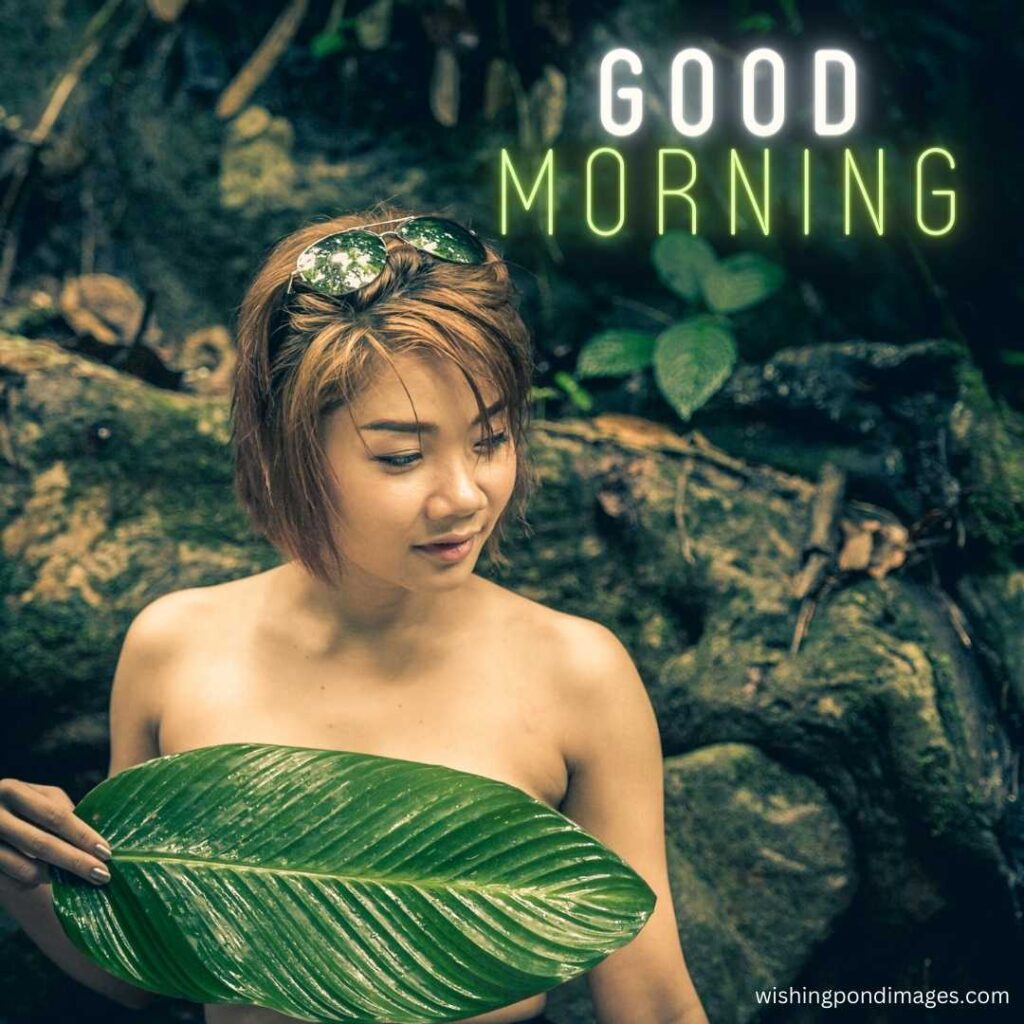 A young girl standing in the forest wearing sunglasses holding a big leaf in her right hand looking at her left side in the morning