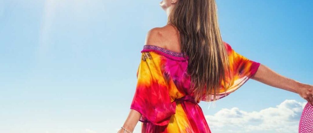 A young girl standing on the beach wearing a colorful dress looking at the sun with closed eyes. Good morning images.