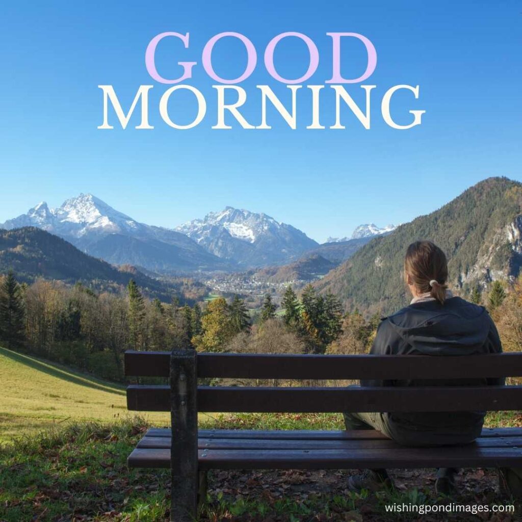 A young man sitting on the bench in the park wearing a black jacket looking at the mountains in the morning