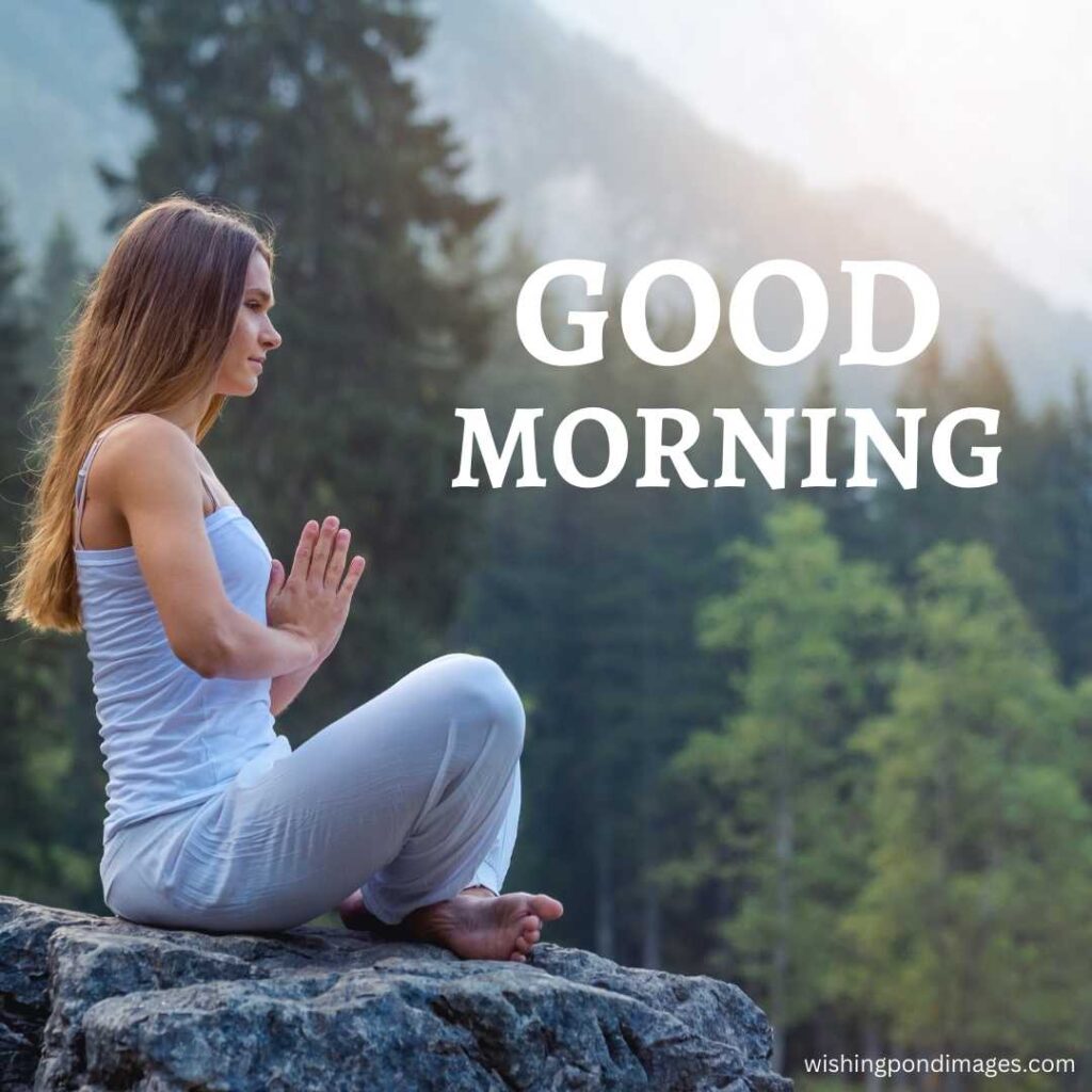 A young woman sitting on the rock in the park in a meditating pose wearing a white sleeveless top and white pajama in the morning