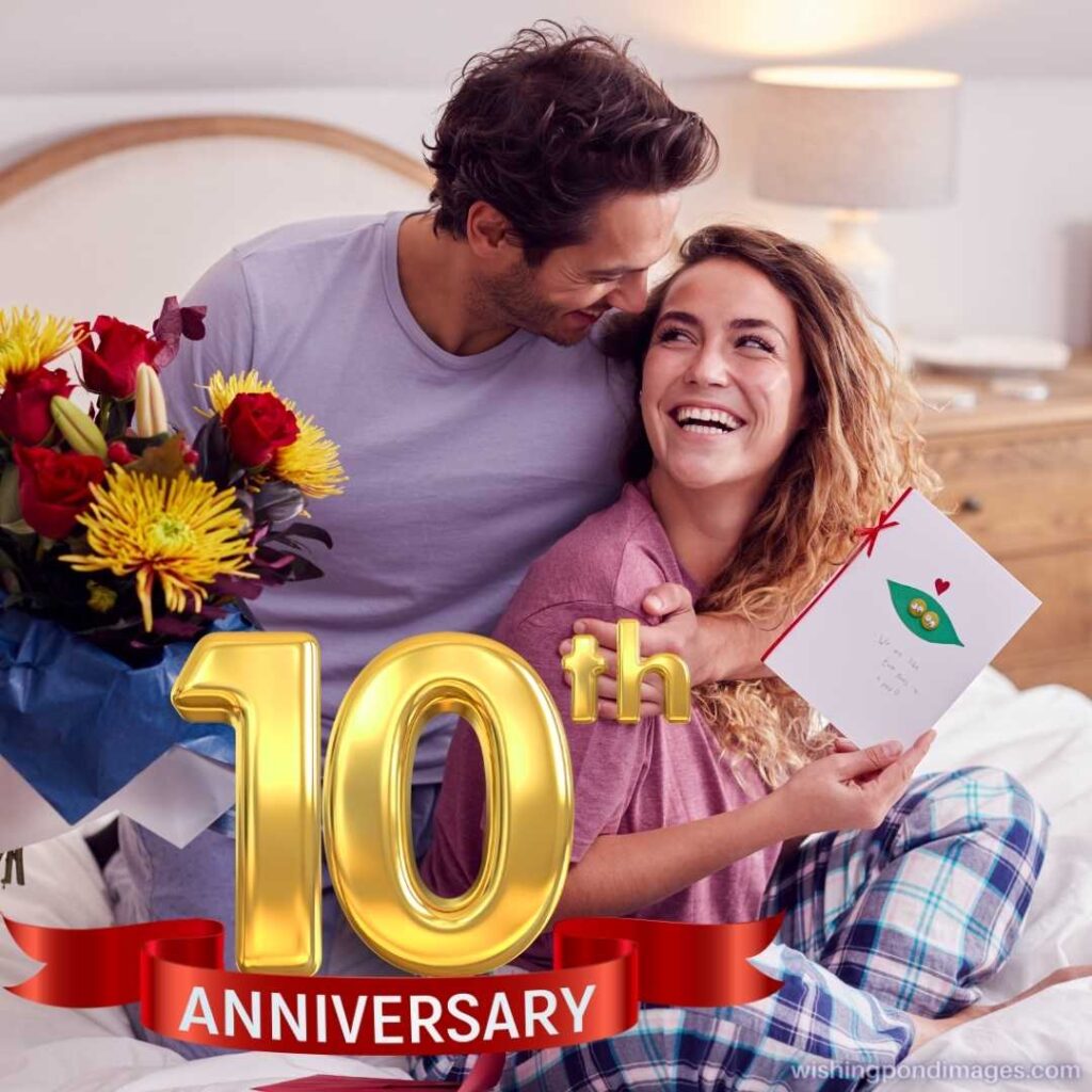 Couple wearing pyjamas in bed at home celebrating anniversary with card and flowers