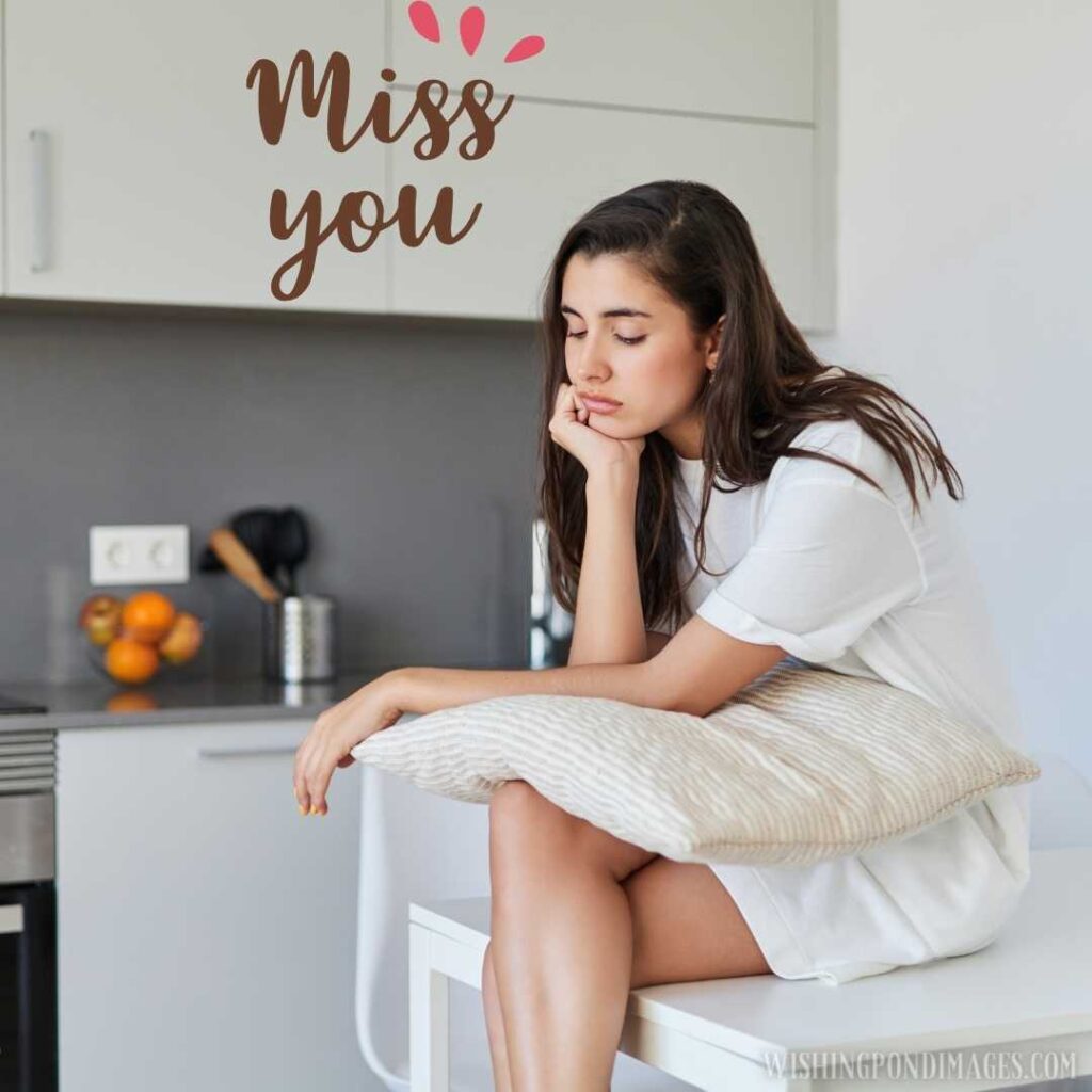 Sad young woman hugging a cushion while sitting at the table in her home