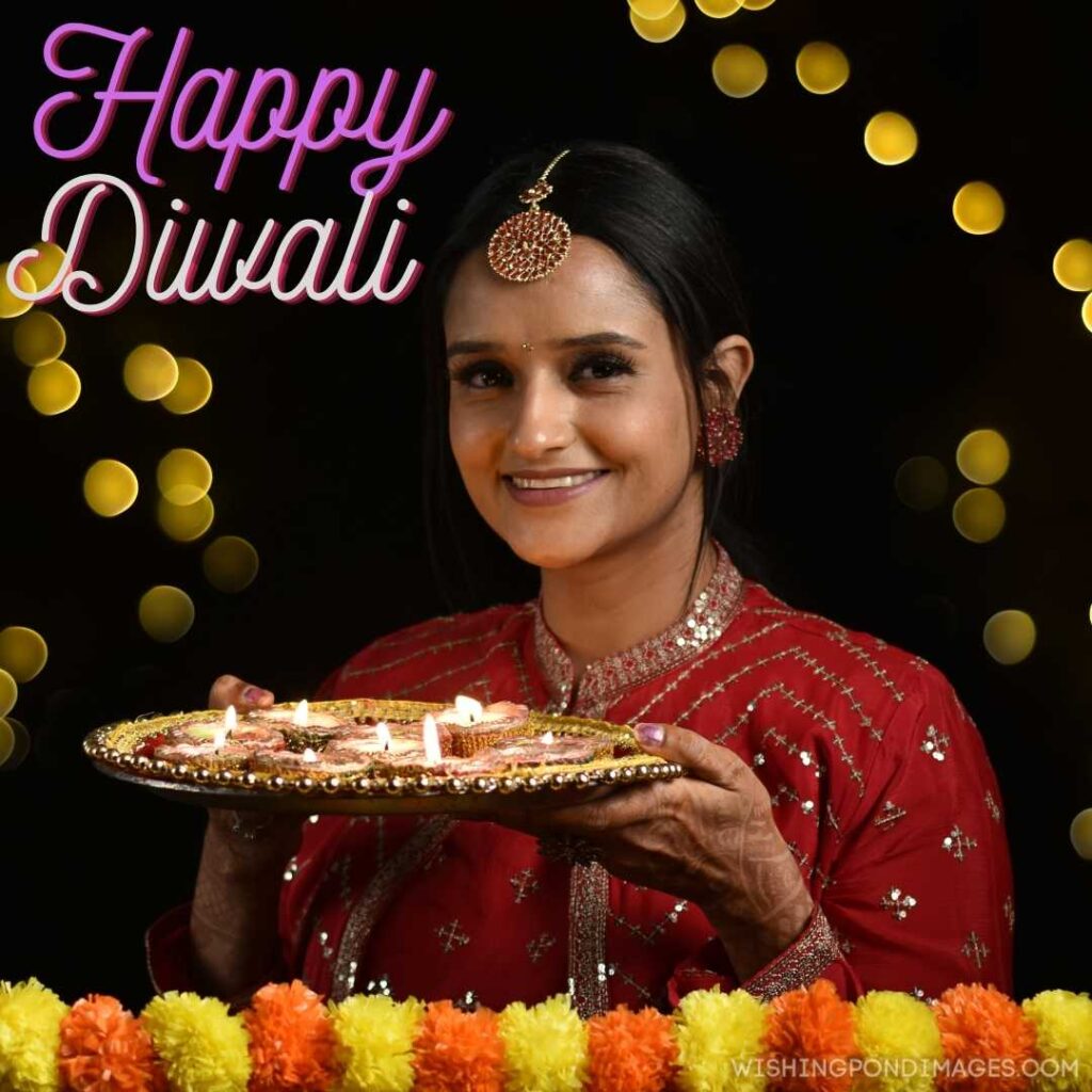 A woman holding decoration plate of diyas and sweets and smiling - Happy Diwali Image