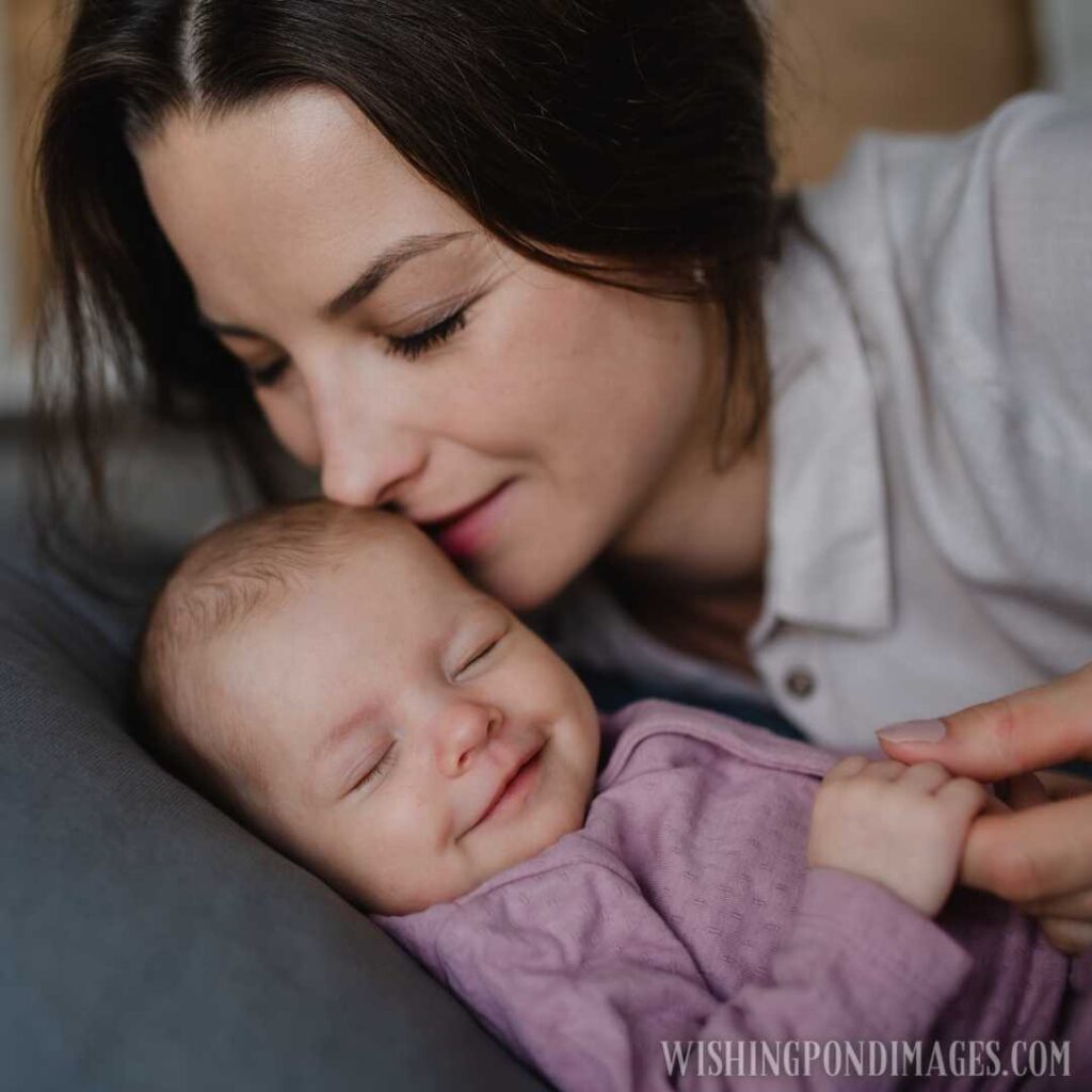 A happy mother kissing her newborn baby, lying on sofa indoors at home. Newborn baby image