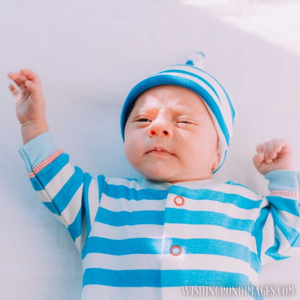 A newborn baby wearing white-blue full-sleeve t-shirt and winter cap looking at front. Newborn baby image