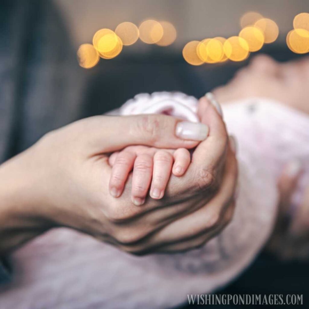Closeup of a newborn baby girl in her mother's hand on a blurred background with bokeh lights. Newborn baby image
