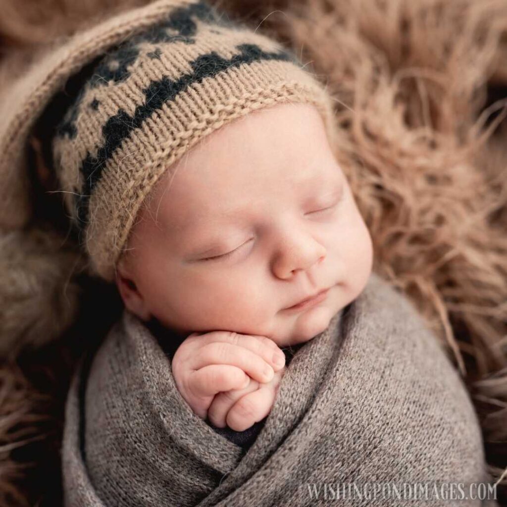 Newborn baby boy swaddled in fabric sleeping and holding his hands close to cheeks. Newborn baby images