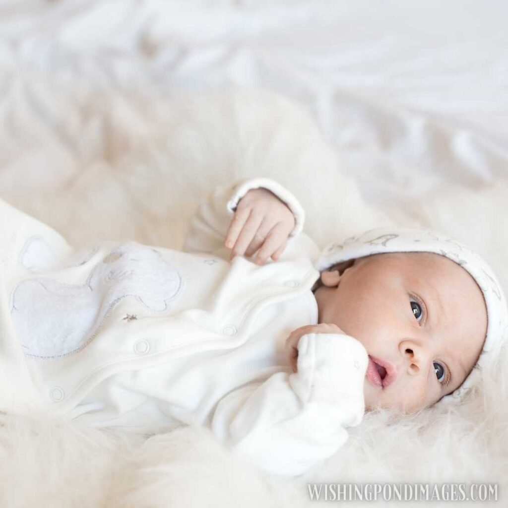 Newborn baby wearing cream-colored suit and winter cap on head, lying on bed. Newborn baby image