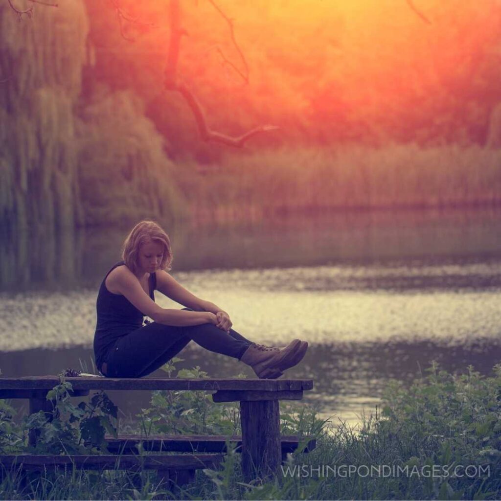 A beautiful young girl sitting on the bench alone near the river. Feeling alone images girl.