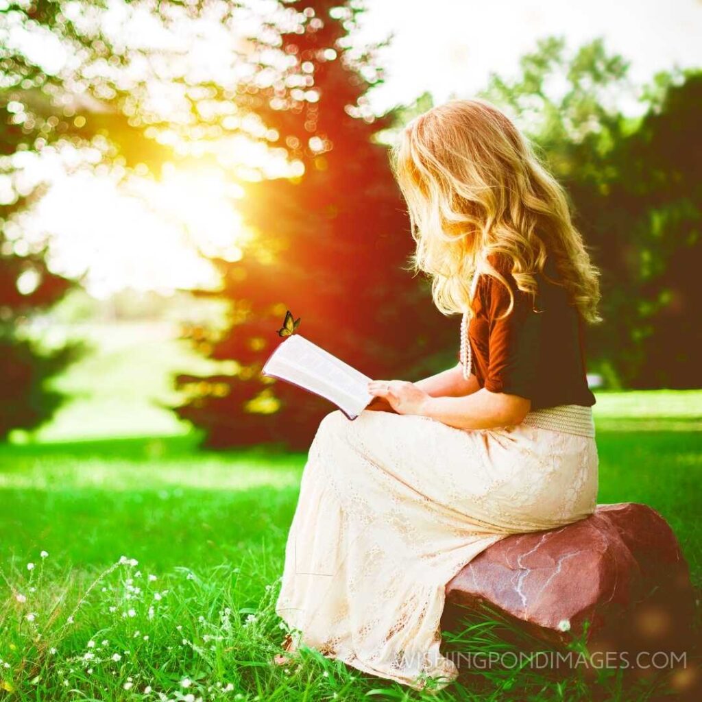 A beautiful young girl sitting on the stone and reading book in the park. Feeling alone images girl.