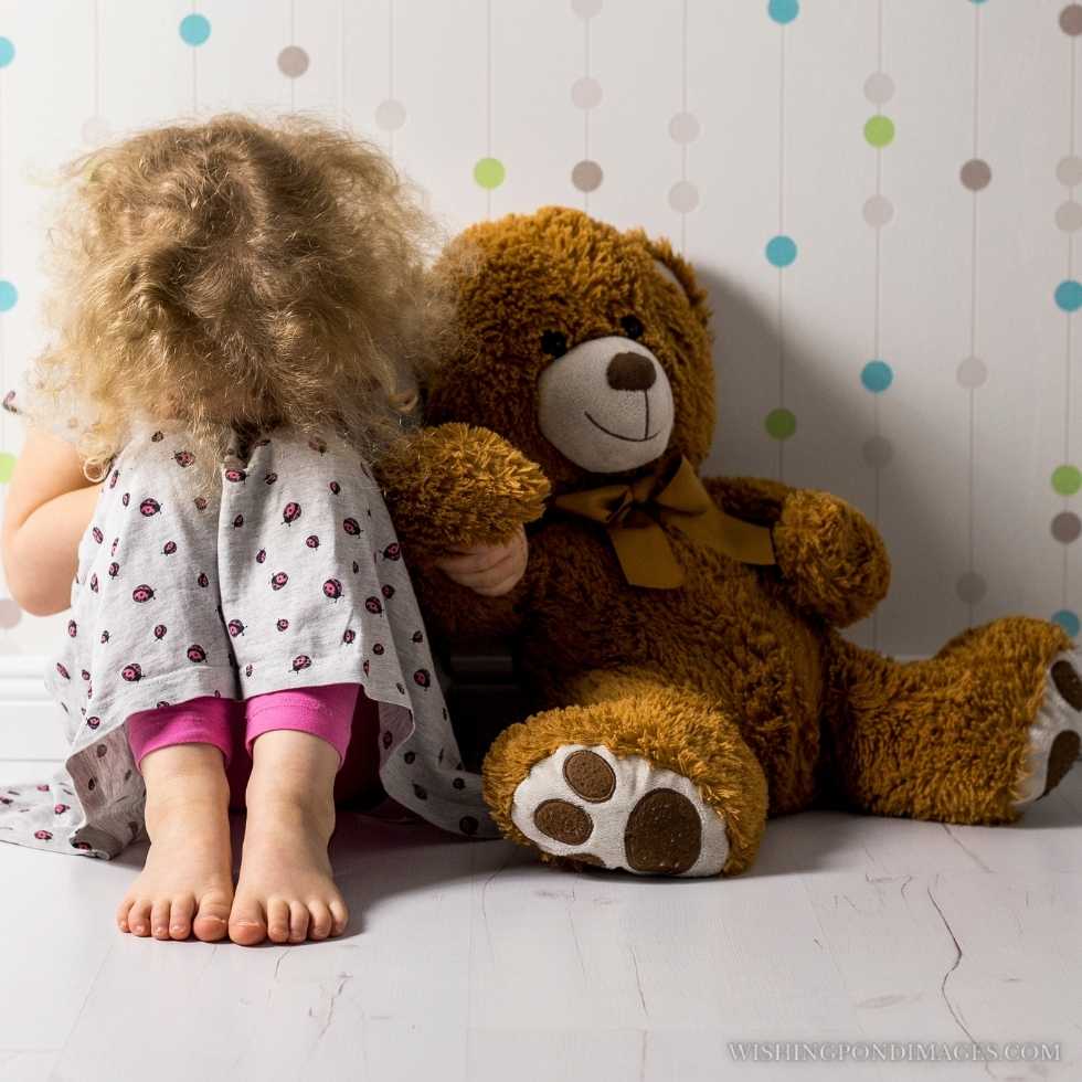 A little sad girl sitting in her room with a teddy bear. Sad girl in room.