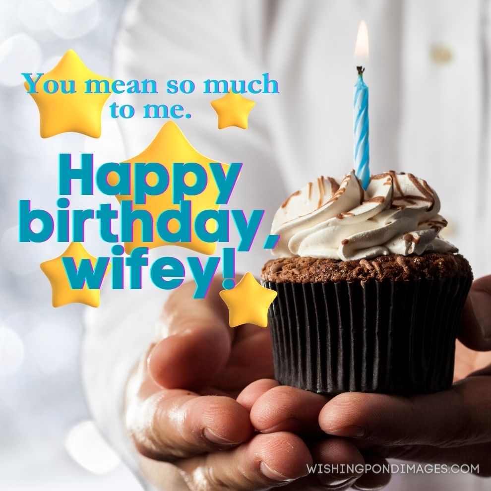 A man holding a cupcake with a candle in a silver lights background. Happy birthday wife images.