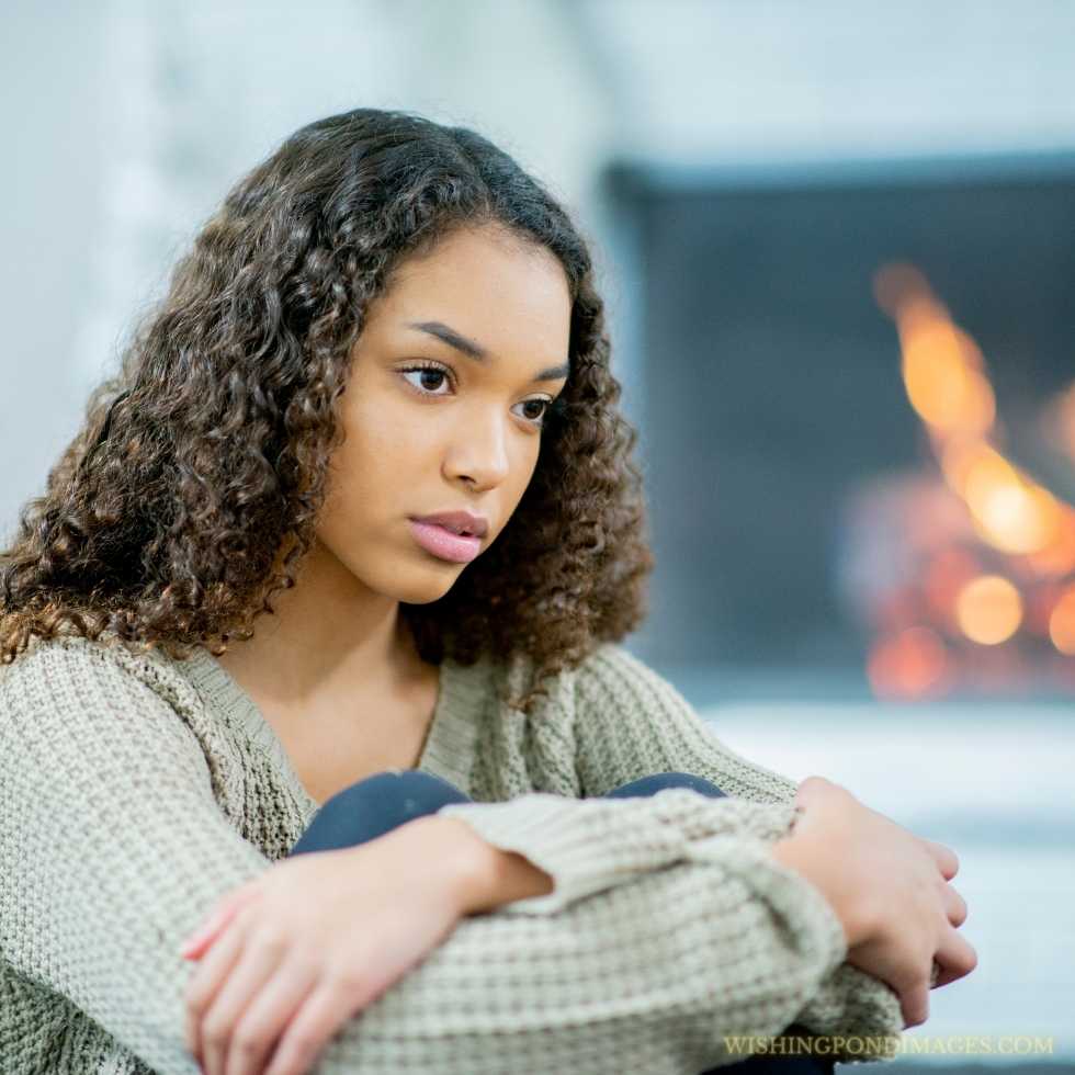 A teenage girl of African descent is in her room sitting on the floor and looking lonely. Sad girl in room.