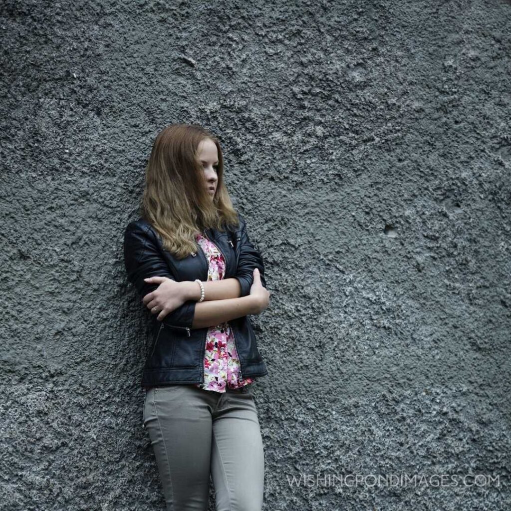 A young beautiful blonde girl standing against the grey wall background. Feeling alone images girl.