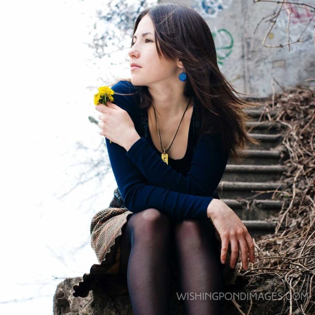 A young beautiful girl sitting alone holding flowers in her hands. Feeling alone images girl.