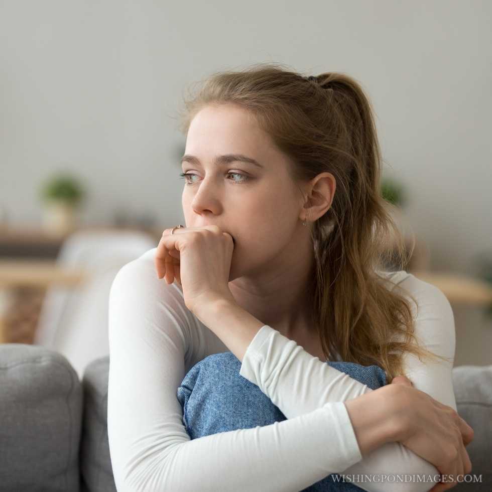 An anxious worried woman sitting on the couch at home. Sad girl in room.