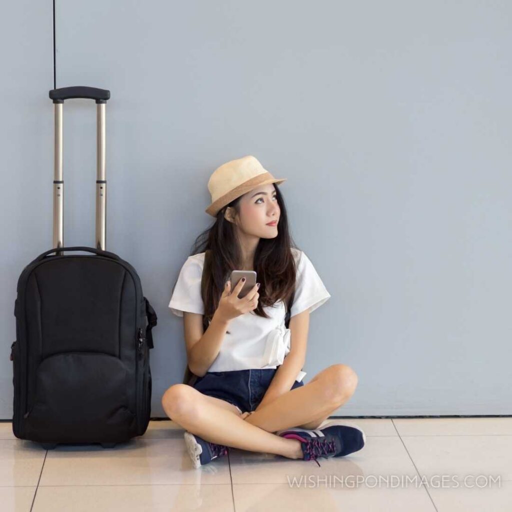 Asian teenager girl using smartphone at airport terminal sitting with luggage suitcase and feeling alone. Feeling alone images girl.