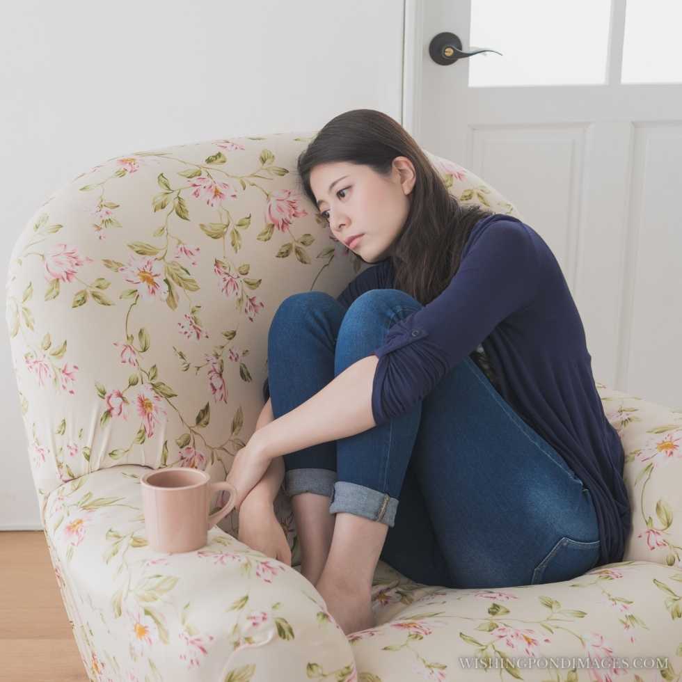 Beautiful elegant woman sitting on living room sofa chair relaxing when she feeling tired. Sad girl in room.