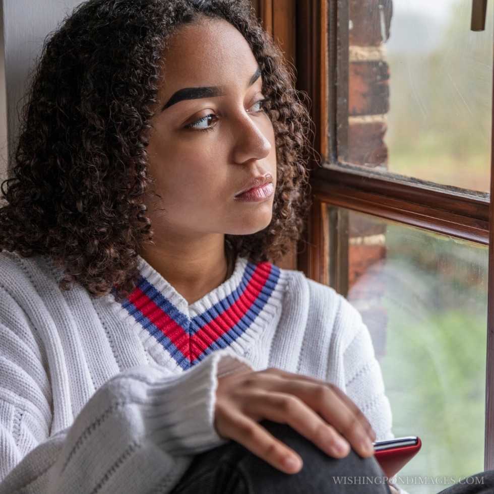 Beautiful mixed-race African-American teenage girl feeling sad sitting in the room near the window. Sad girl in room.