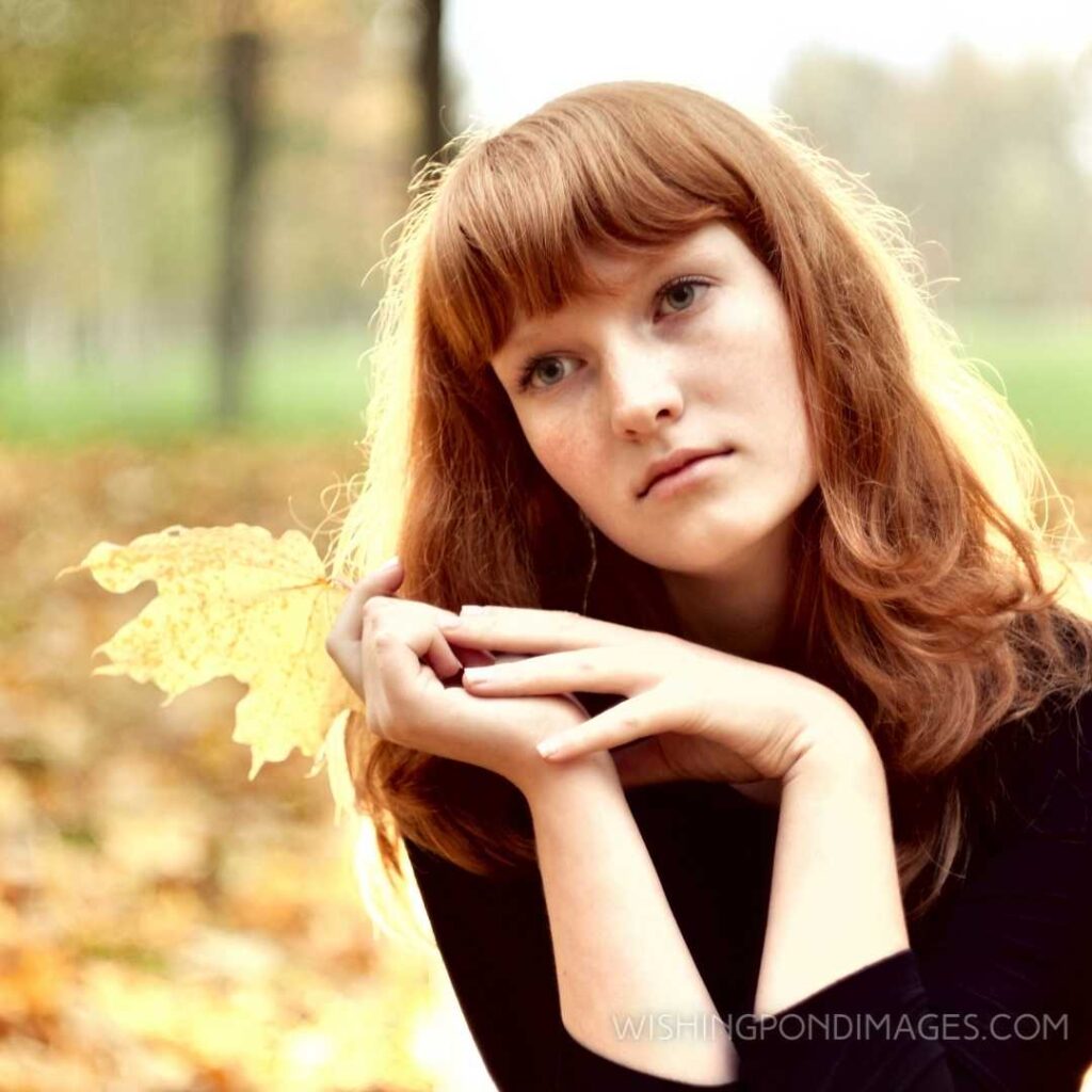 Beautiful red-haired girl sitting alone in autumn park. Feeling alone images girl.