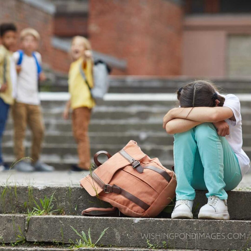 Crying school girl sitting on stairs outdoors with group of teasing children. Feeling alone images girl.