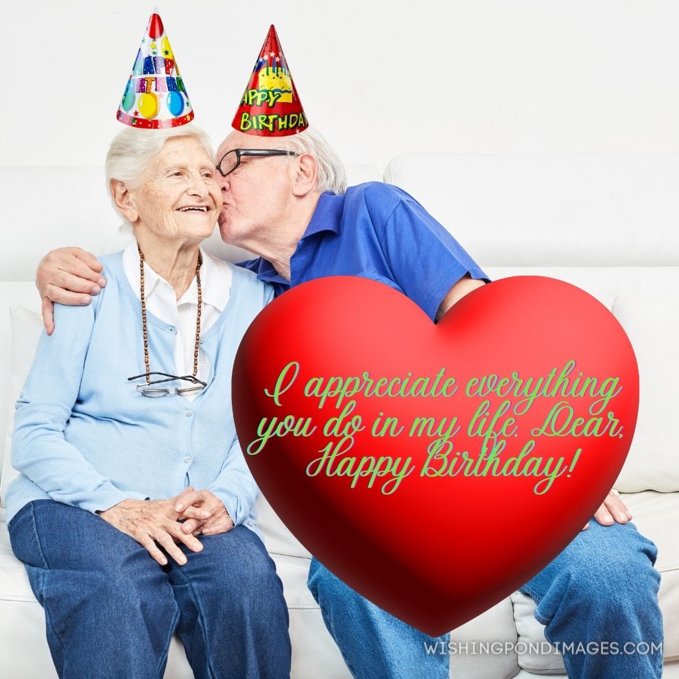 Happy senior hugs and kisses his wife on the sofa at home. Happy birthday wife images.