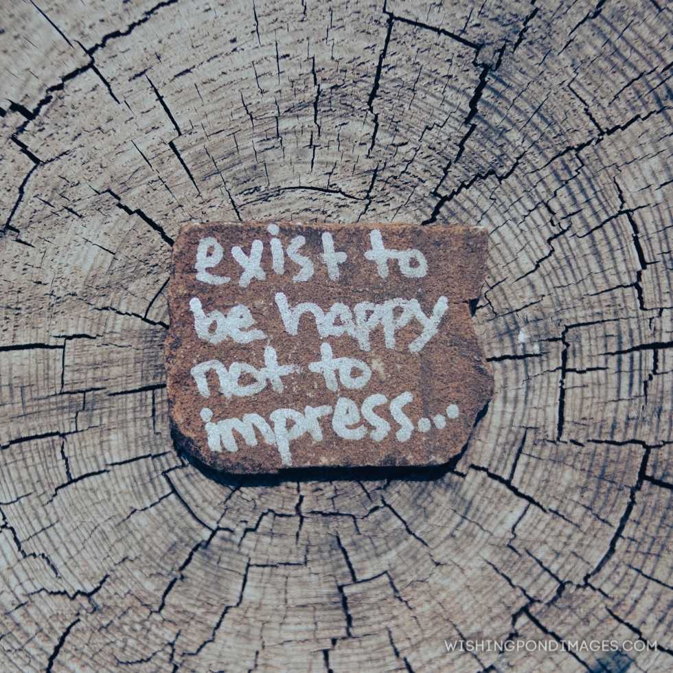 Inspirational words on wooden log - exist to be happy not to impress. Inspirational quotes images