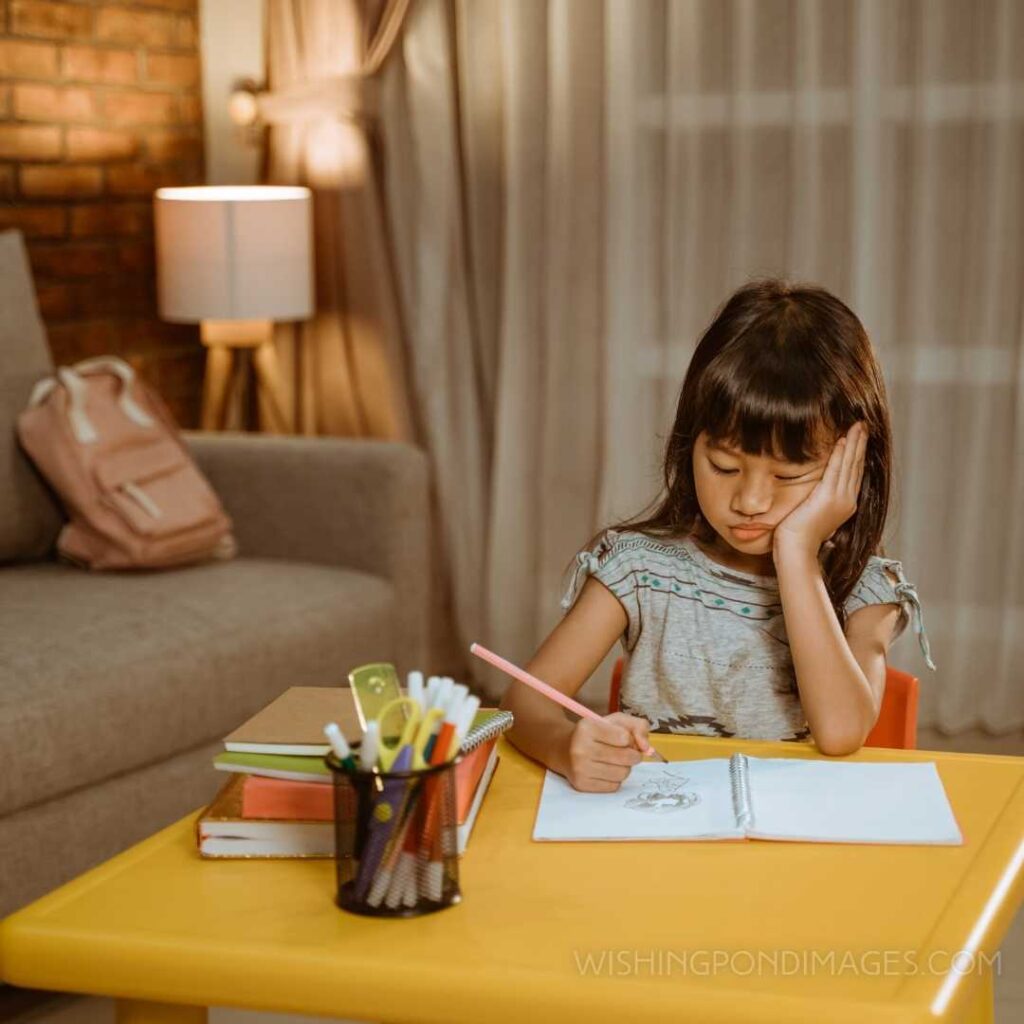 The kid feels bored while doing her homework at home in the evening. Feeling alone images girl.