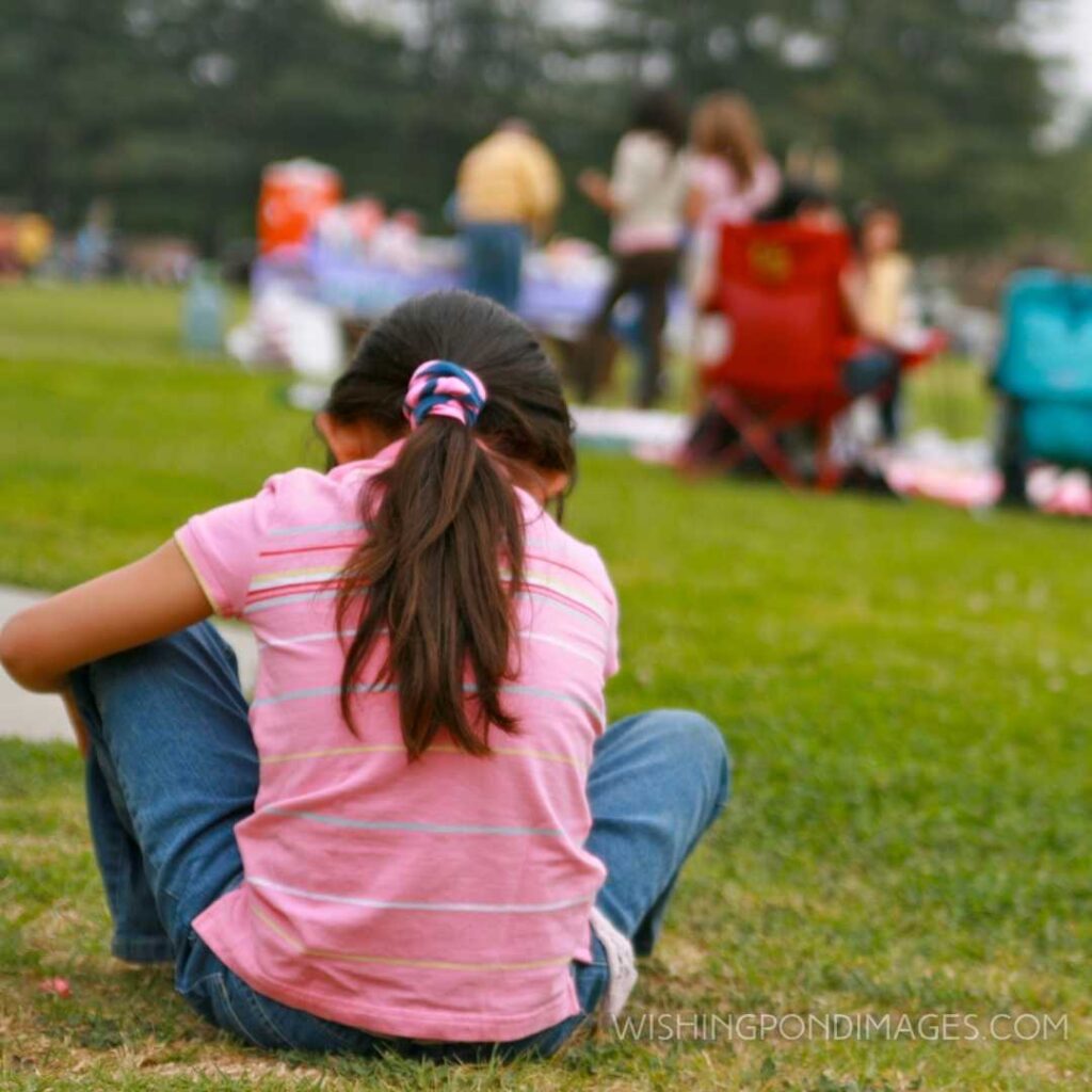 A little girl sits alone while her family and friends are enjoying a picnic together on Easter Sunday. Feeling alone images girl.