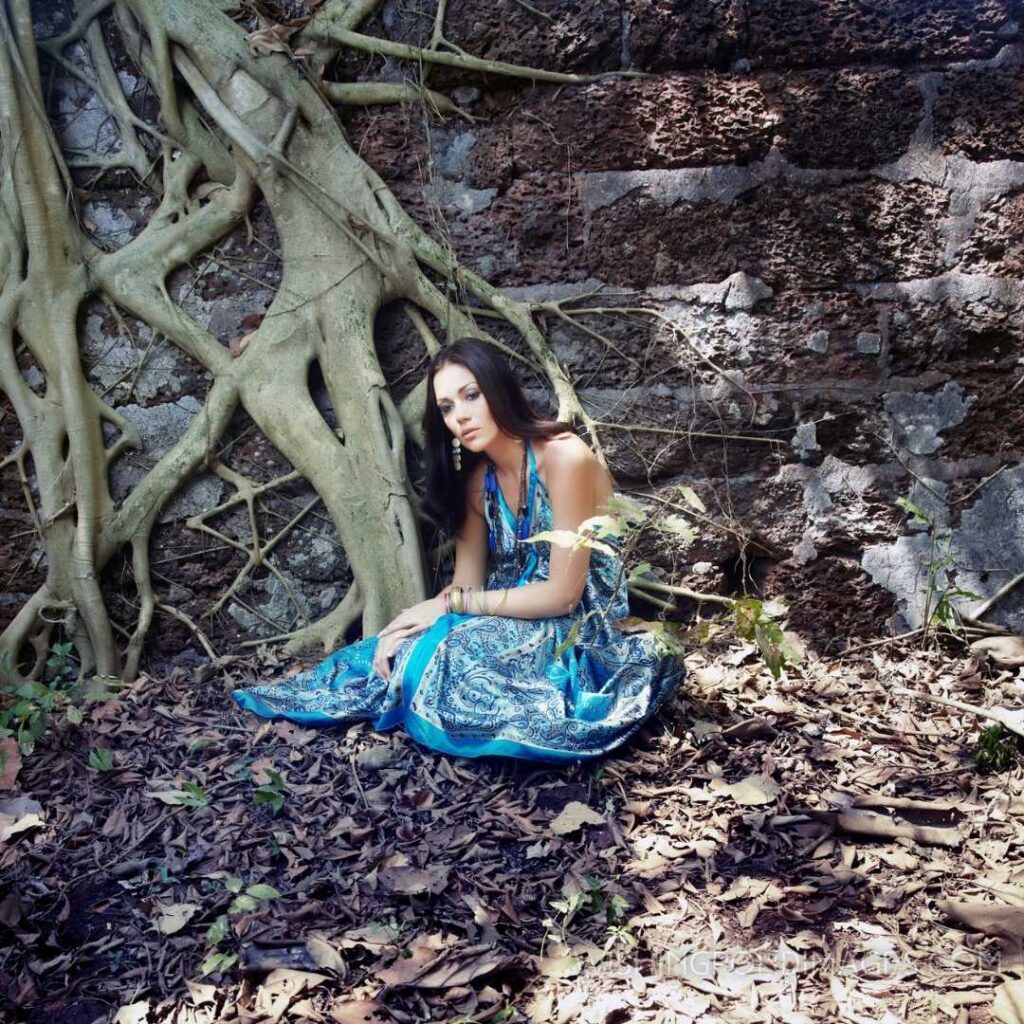 Lonely woman in the blue dress sitting near the old stony wall and banyan. Feeling alone images girl.