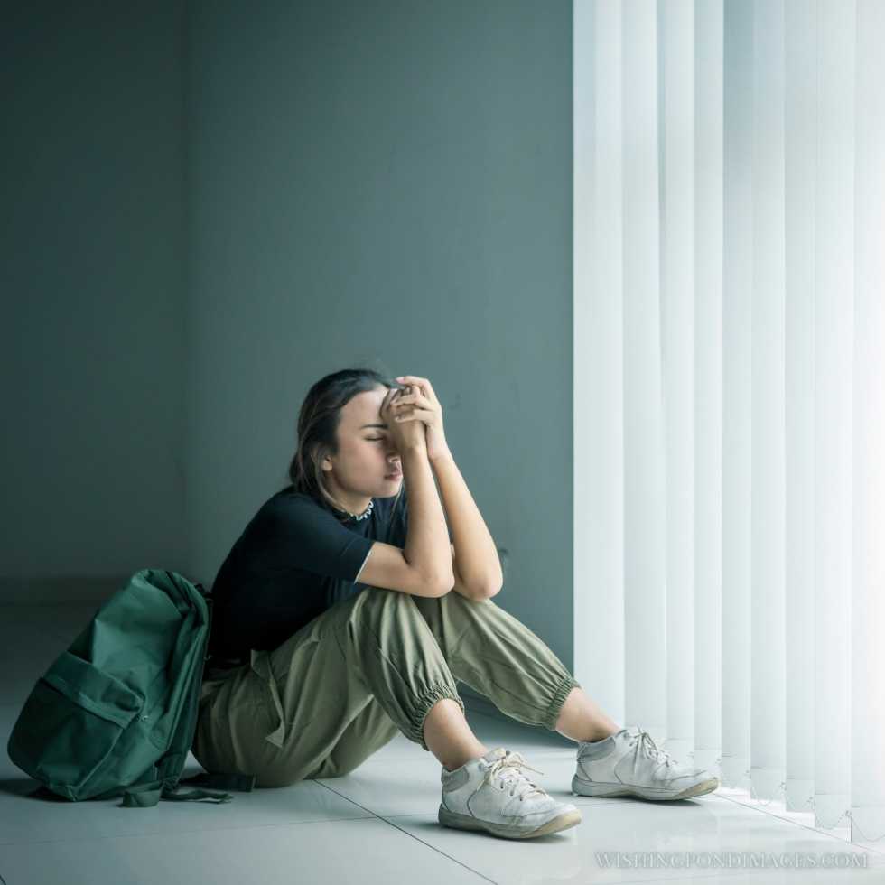 Picture of a teenage girl sitting near the window with a sad expression. Sad girl in room.