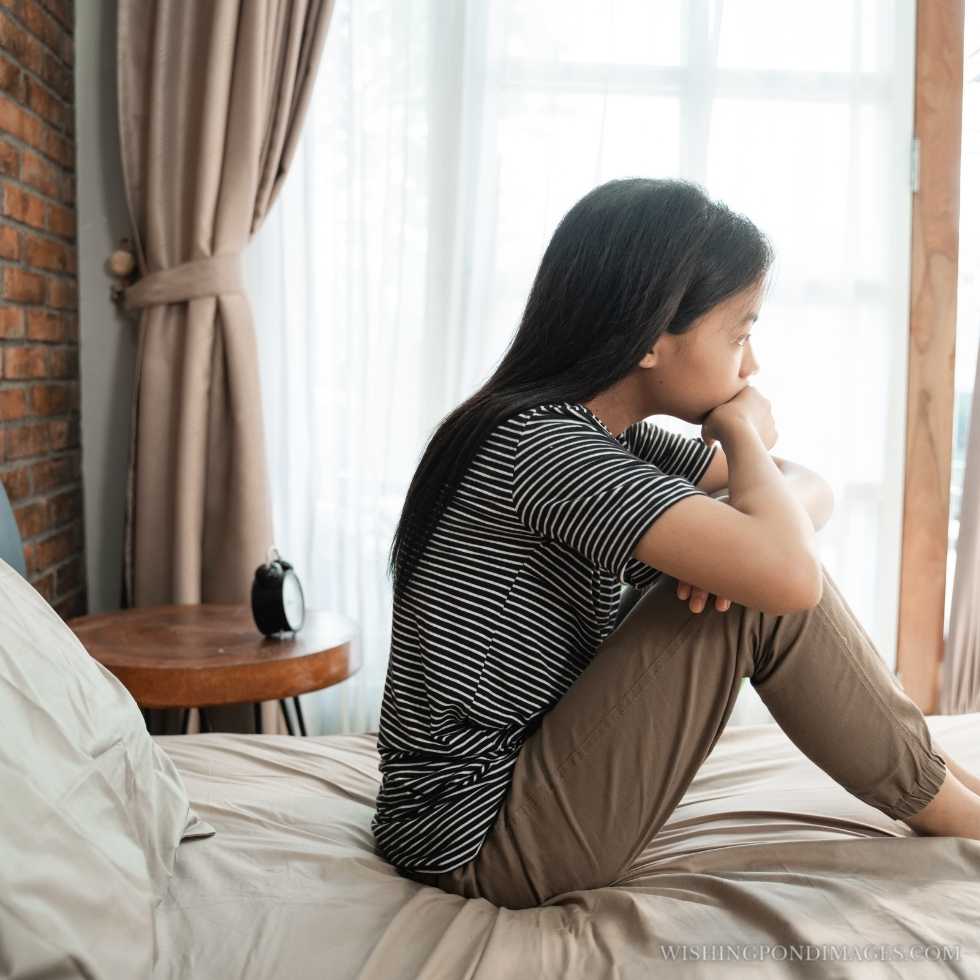 Portrait of an Asian sad teenage girl sitting on the bed. Sad girl in room.