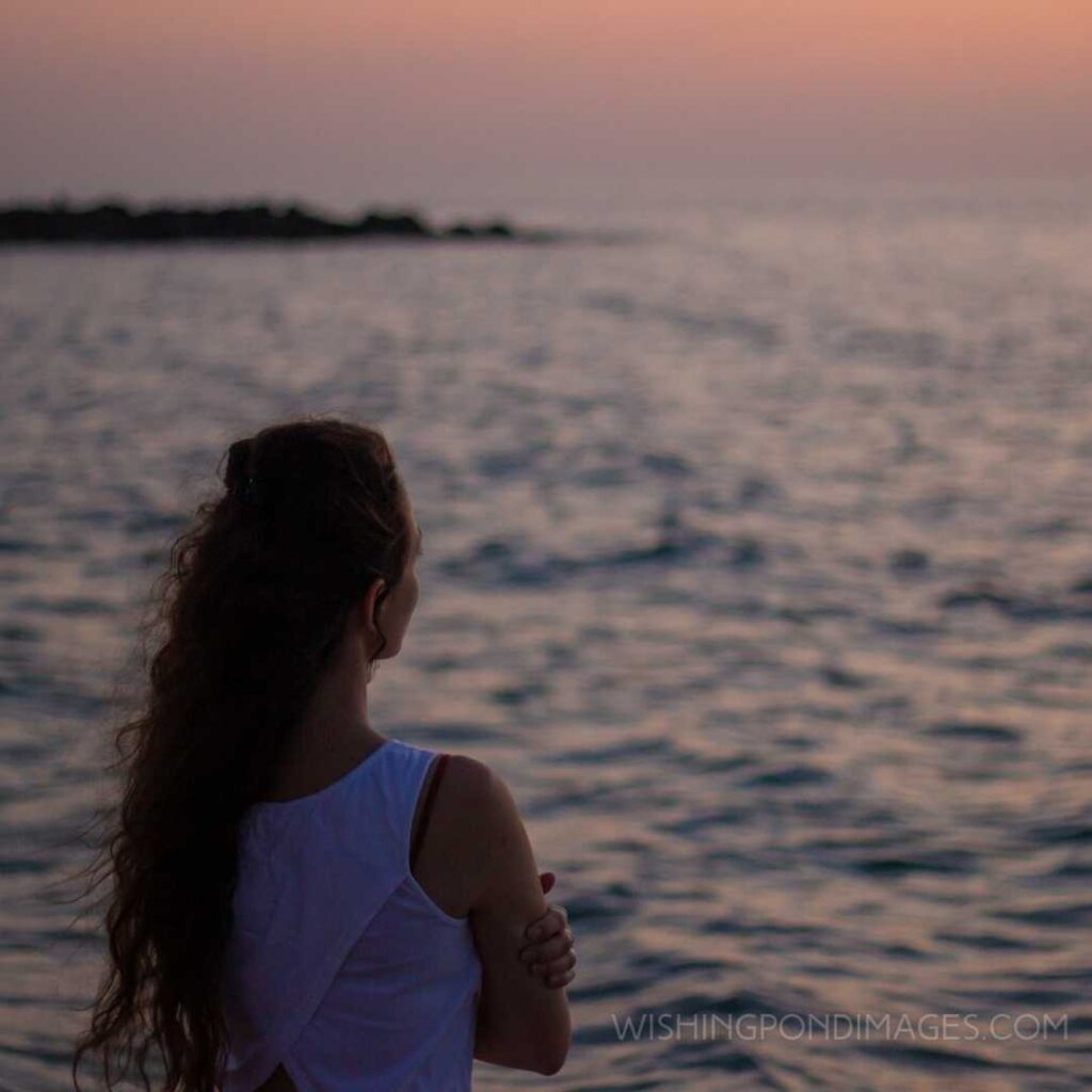 A pretty girl standing at the beach and looking at the sea during sunset. Feeling alone images girl.