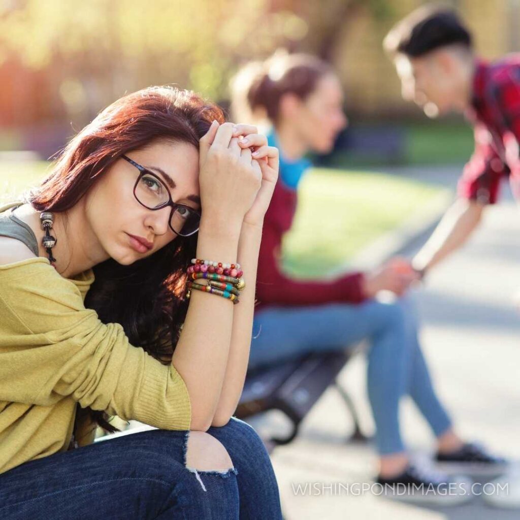 Red haired girl sitting on the bench and looking at the camera. Feeling alone images girl.
