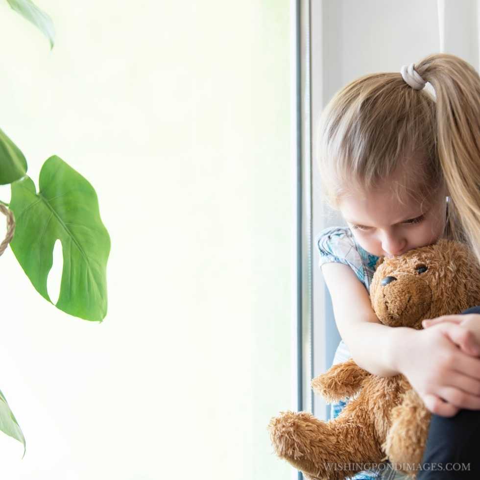 Sad child girl by the window at home. Sad girl in room.