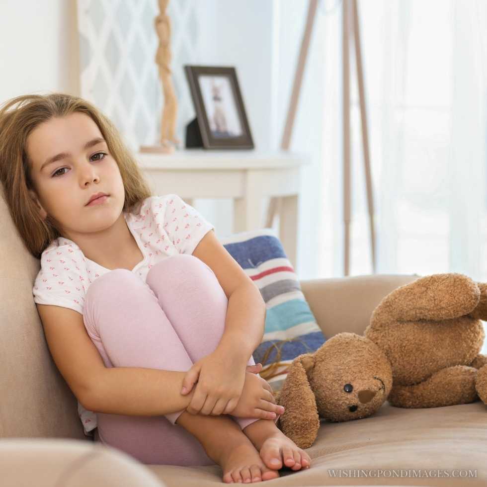 Sad little girl sitting on the couch in room. Sad girl in room.