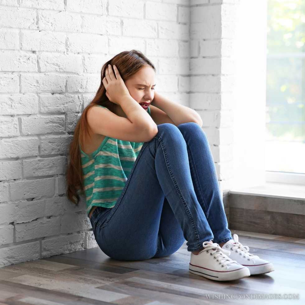 Sad teenage girl sitting near window in a room. Sad girl in room.