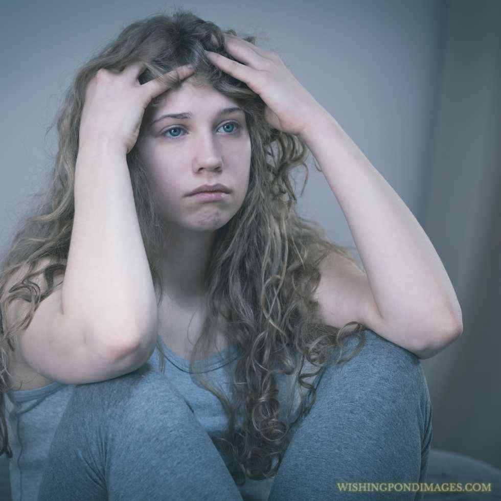 A sad teenager sitting alone in a gray room. Sad girl in room.