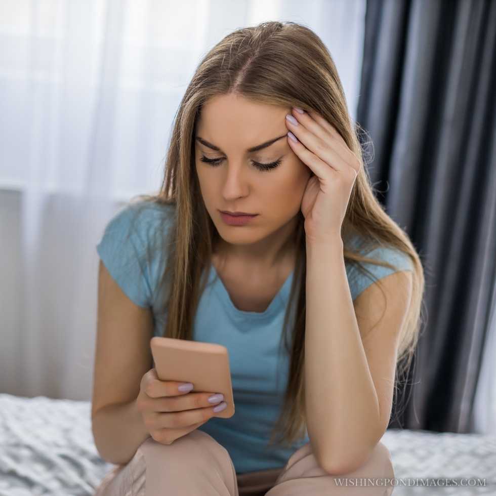 A sad woman holding the phone while sitting on the bed in her bedroom. Sad girl in room.