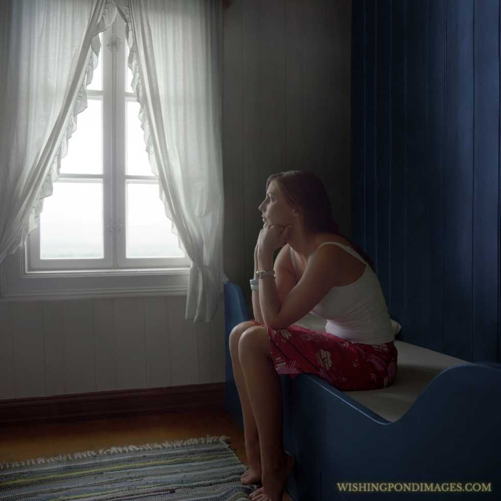 Side view of a young thoughtful sad woman sitting alone in the room. Sad girl in room.