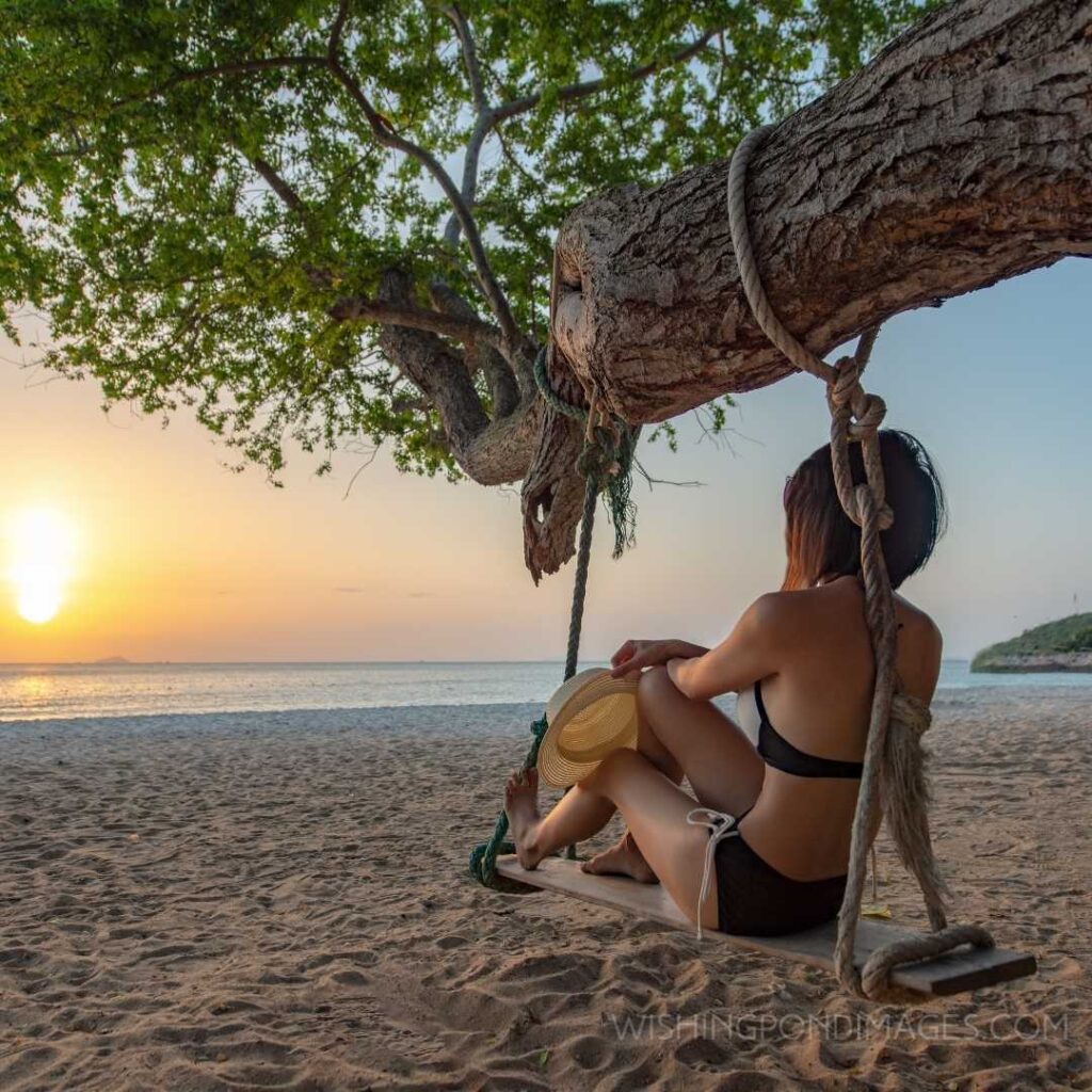 Woman in bikinis enjoys the sunset by sitting on wooden swings on the sea search alone. Feeling alone images of girl.
