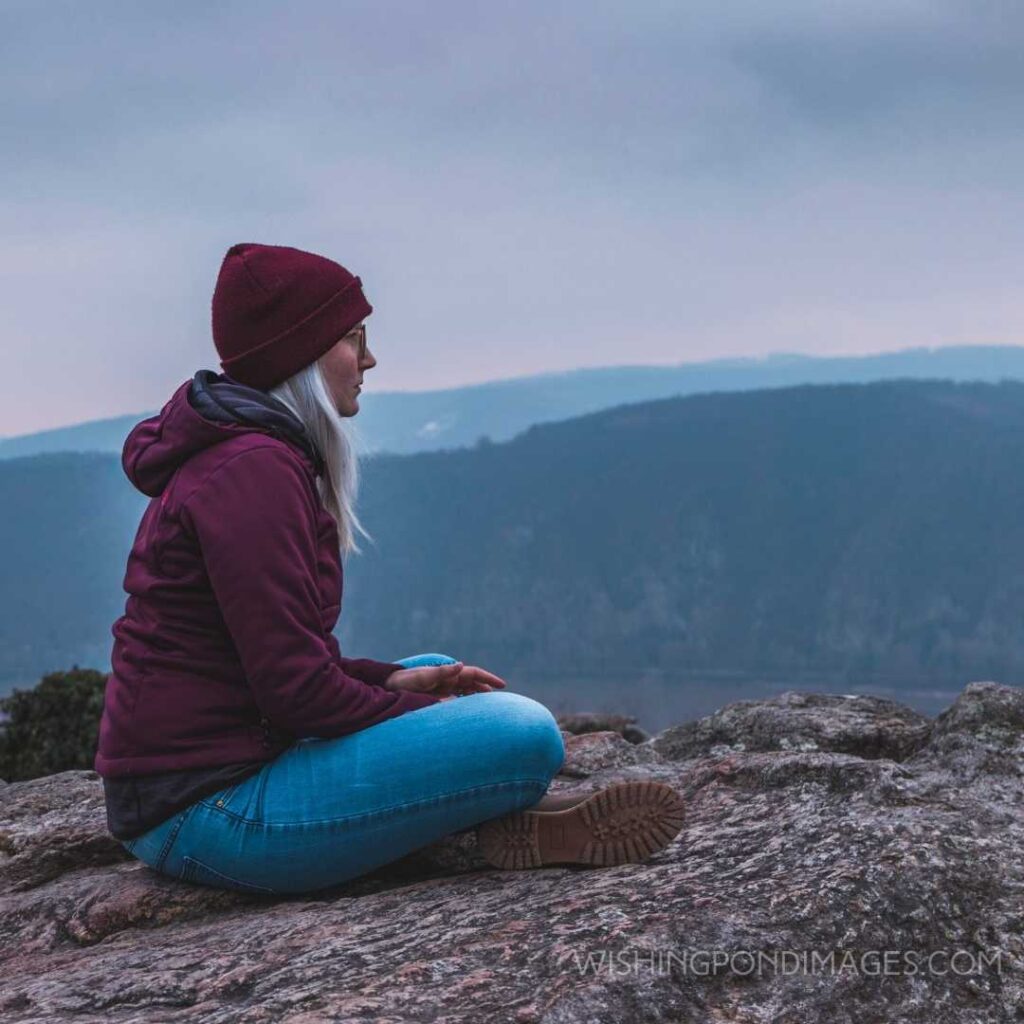 Woman sitting on the ground watching over mountains. Feeling alone images of girl