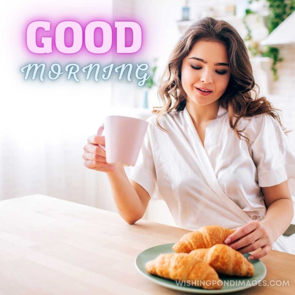 Young Woman with dark hair sitting in kitchen and drinking coffee in Morning taking one croissant and smile. Good Morning Coffee Images