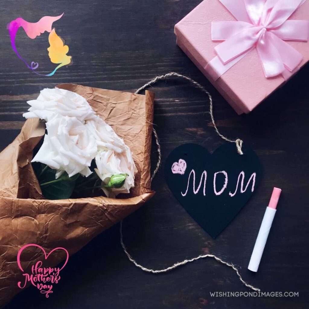 Mom written on black-shaped heart with white flowers beautiful bouquet and pink gift box on dark wooden table. Happy Mothers Day images