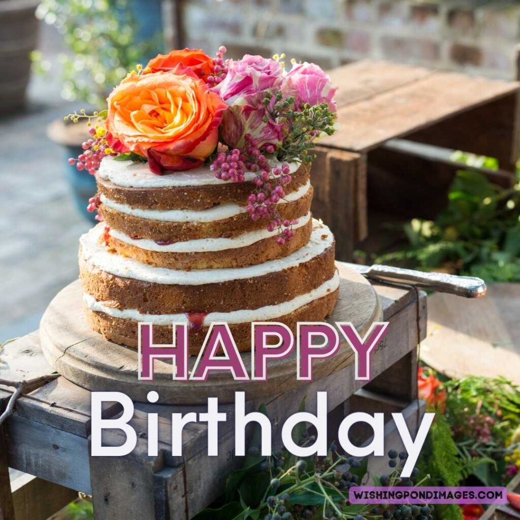 A beautiful sponge layered cake with colorful cakes on top sitting on a wooden box table. Happy birthday cake flowers images