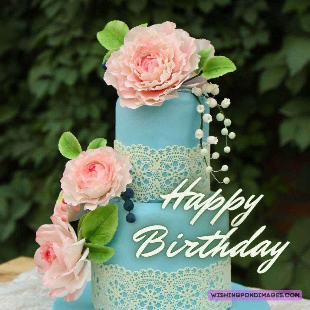 A two-layered sky blue colored cake with pink flowers with leaves on a natural background. Happy birthday cake flowers images